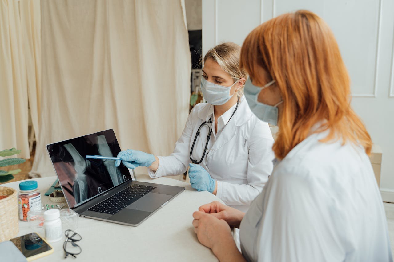 Doctor explains X-ray results to patient using a laptop in a clinic setting.